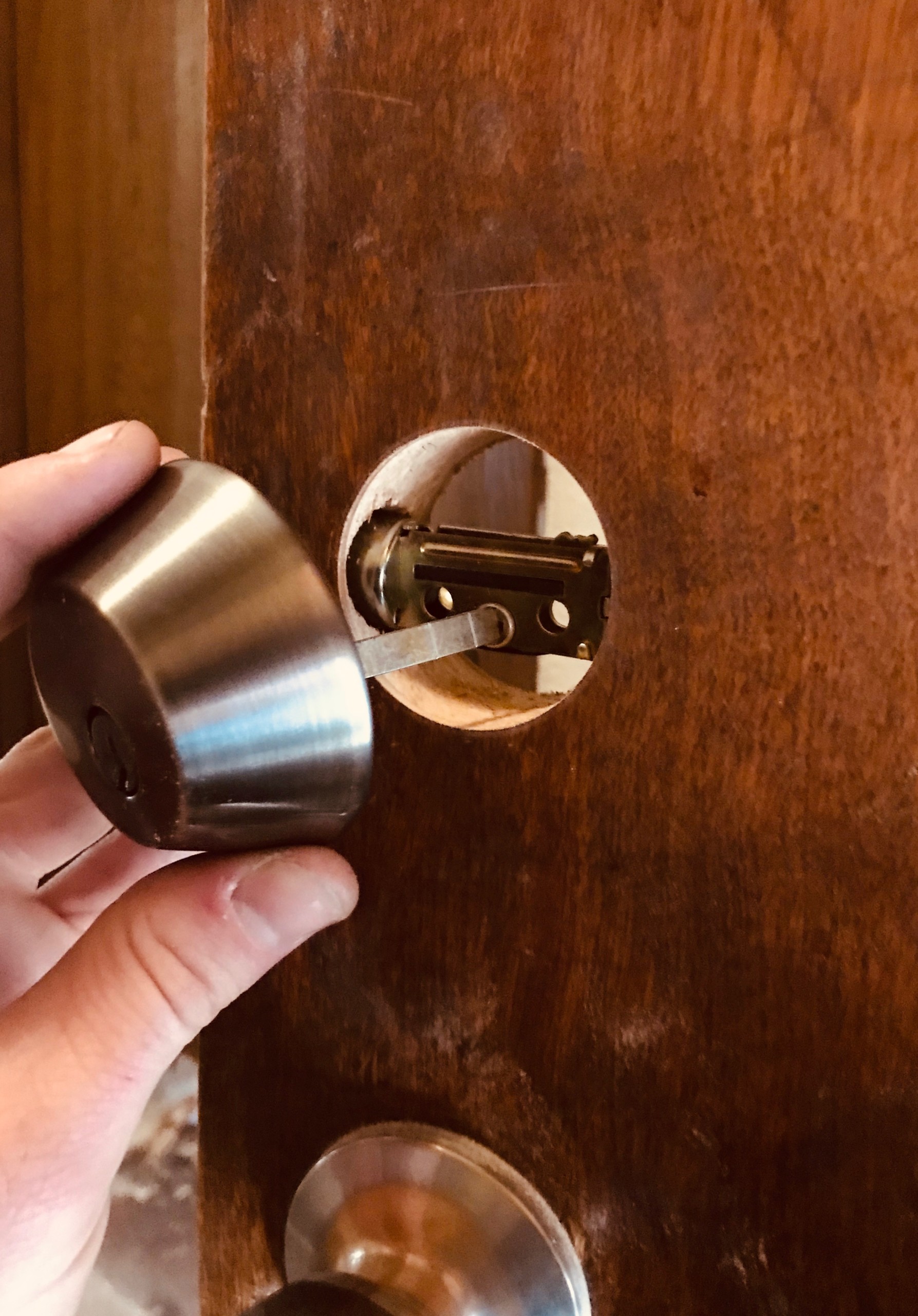 A hand installing a deadbolt onto a wooden door.